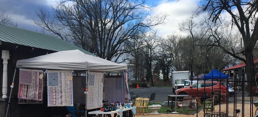 A vendor's stall at an outdoor flea market, quilts and smalls hung up for sale.